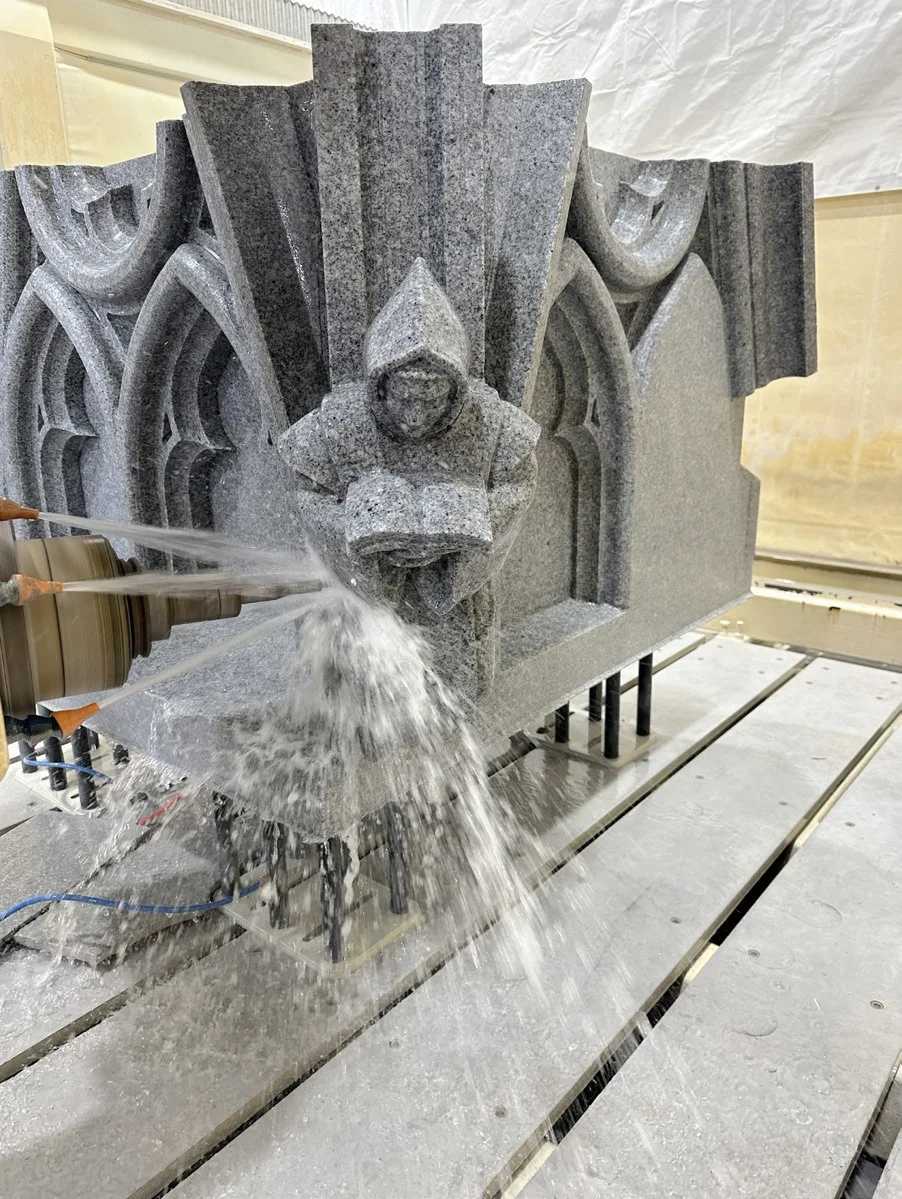 A CNC machine spraying water while carving an intricate granite pinnacle with a hooded monk figure