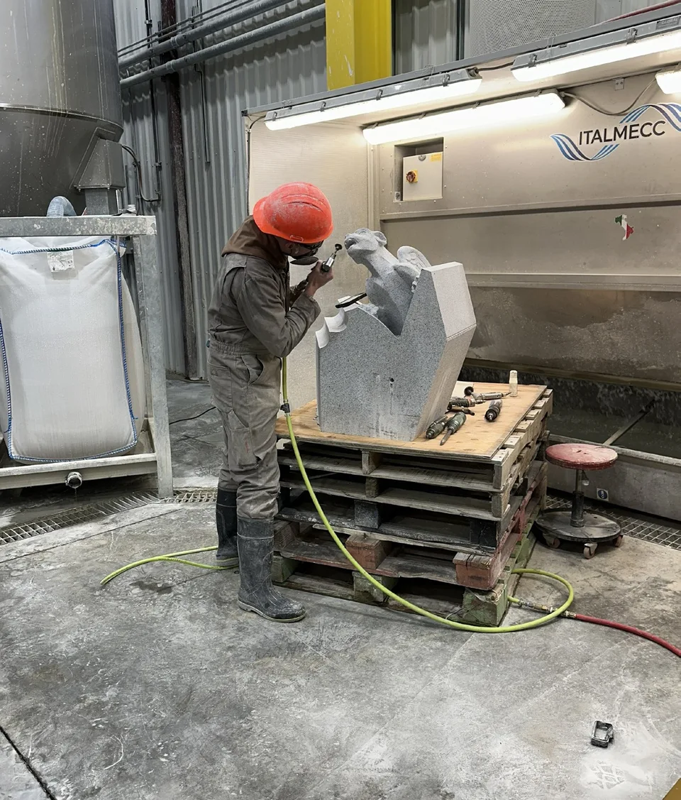A monk wearing a red hard hat carving a granite pinnacle piece in the workshop