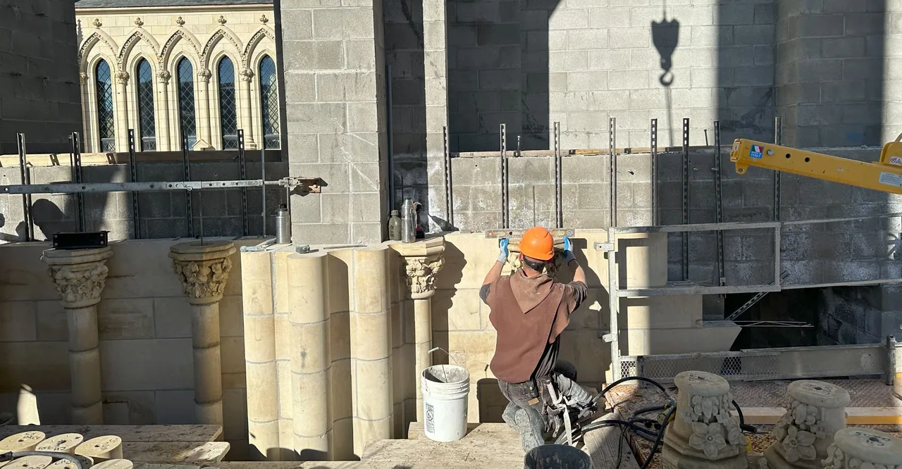A monk setting stone on the Chapel, with carved capitals in the foreground